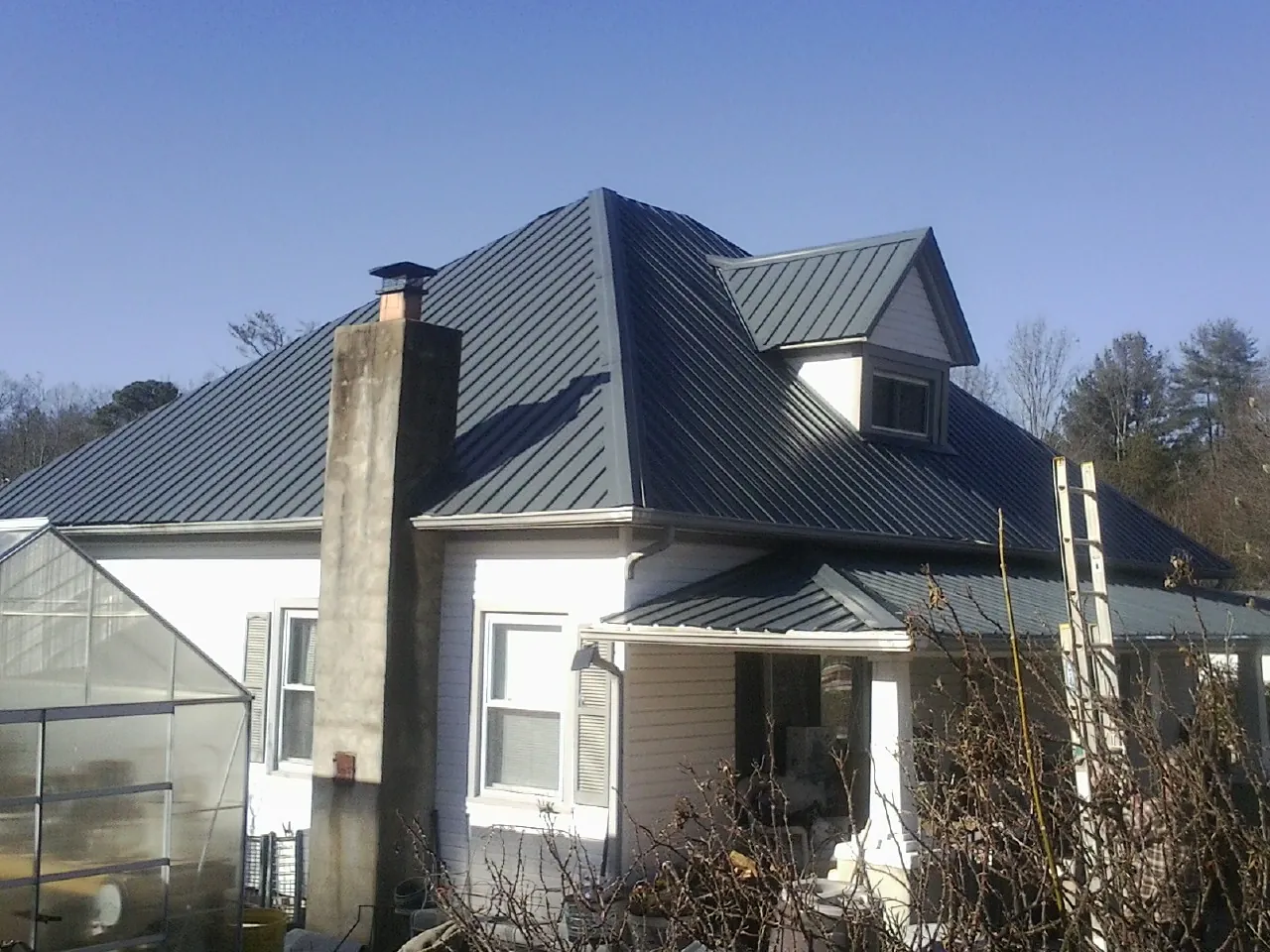Dark blue standing seam metal roof on a white farmhouse with dormer — Slate & Tile Roof Repair by Roofing Brothers in New Port Richey