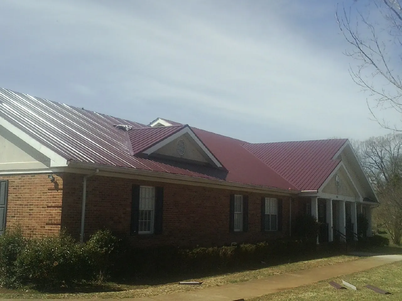 Red metal roof with gabled entries on a long brick building, from a Hail Damage Roof Repair job in New Port Richey