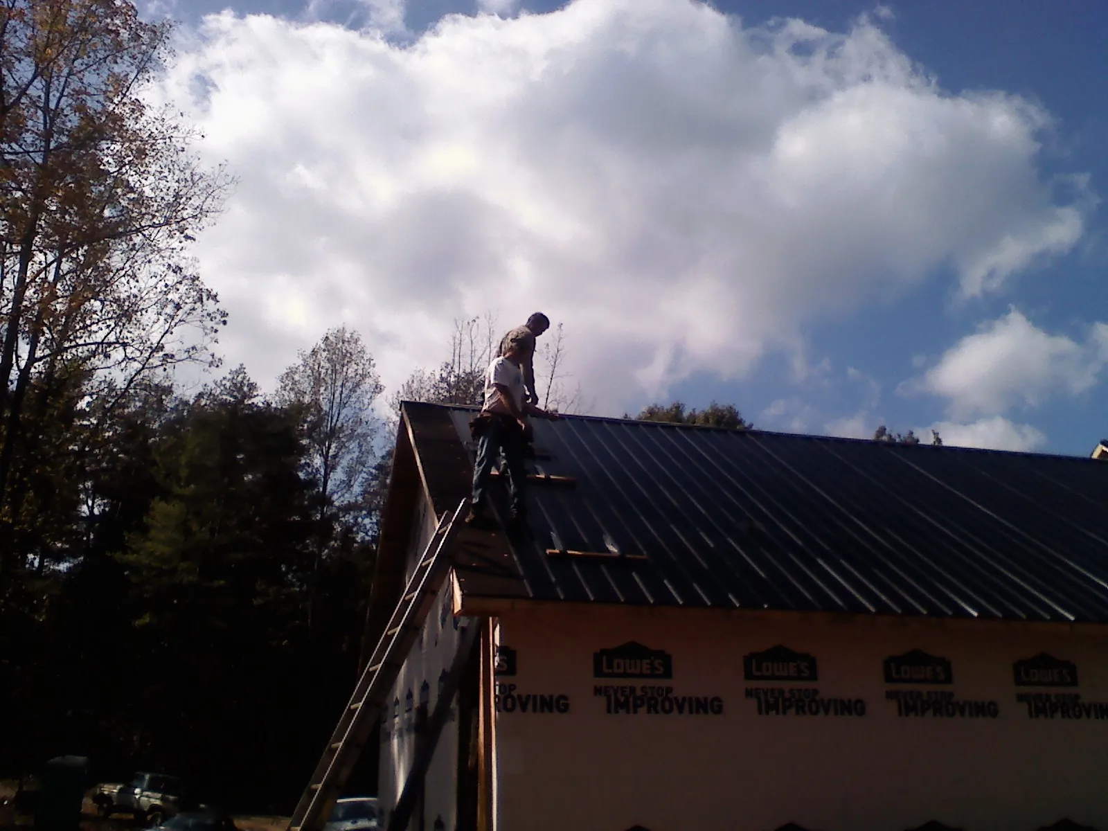 Roofer fastening dark metal panels high against a cloudy sky, from a Roof Inspection job in New Port Richey