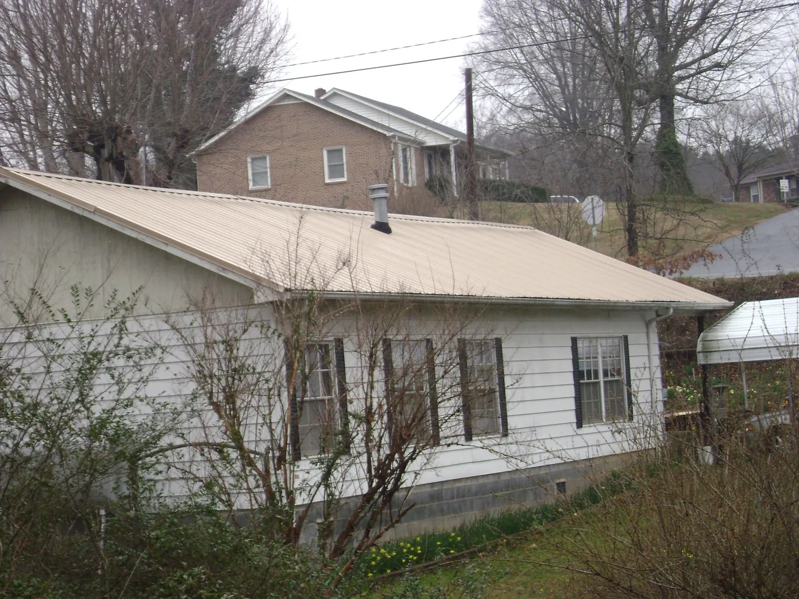 Tan metal roof on a white sided house set into a hillside — Commercial Roofing by Roofing Brothers in New Port Richey